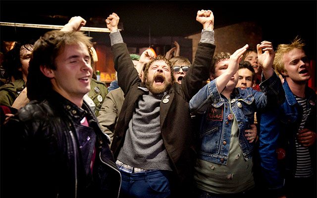 A man raises his fists in the air in exuberant celebration, surrounded by a large group.