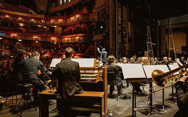 The Orchestra of Opera North performing on stage in Leeds Grand Theatre; a large group of classical musicians sitting together with instruments.