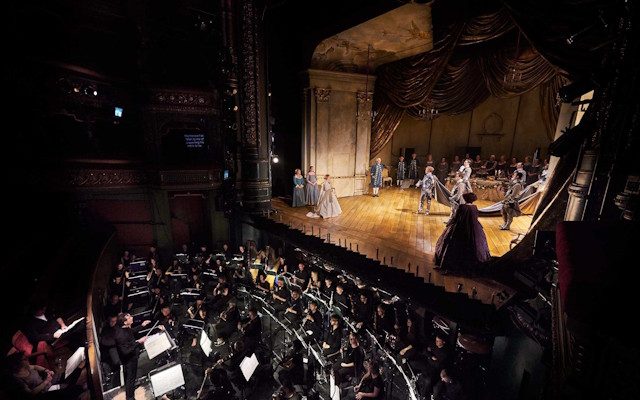 Opera singers rehearsing on stage, in front of an orchestra inside Leeds Grand Theatre.