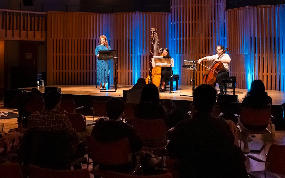 Three musicians performing on stage in front of an audience in the Howard Assembly Room.