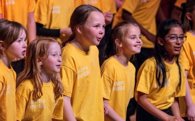 Children aged 7 to 10 in yellow t-shirts singing