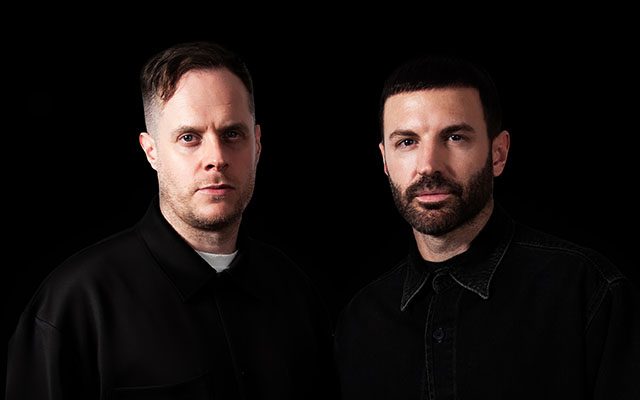 Two men look direct to camera on a dark background.