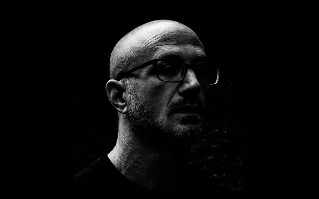 Shadowy photo of a man with glasses against a dark background